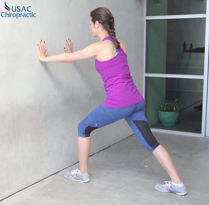 Giãn mở cơ bắp đúng cách bằng cách tựa tay vào tường, duỗi thẳng chân sau